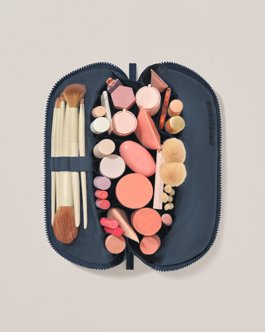 Overhead view of the Medium Indigo (Navy) Traveller makeup bag fully packed with upright beauty products and organized compartments