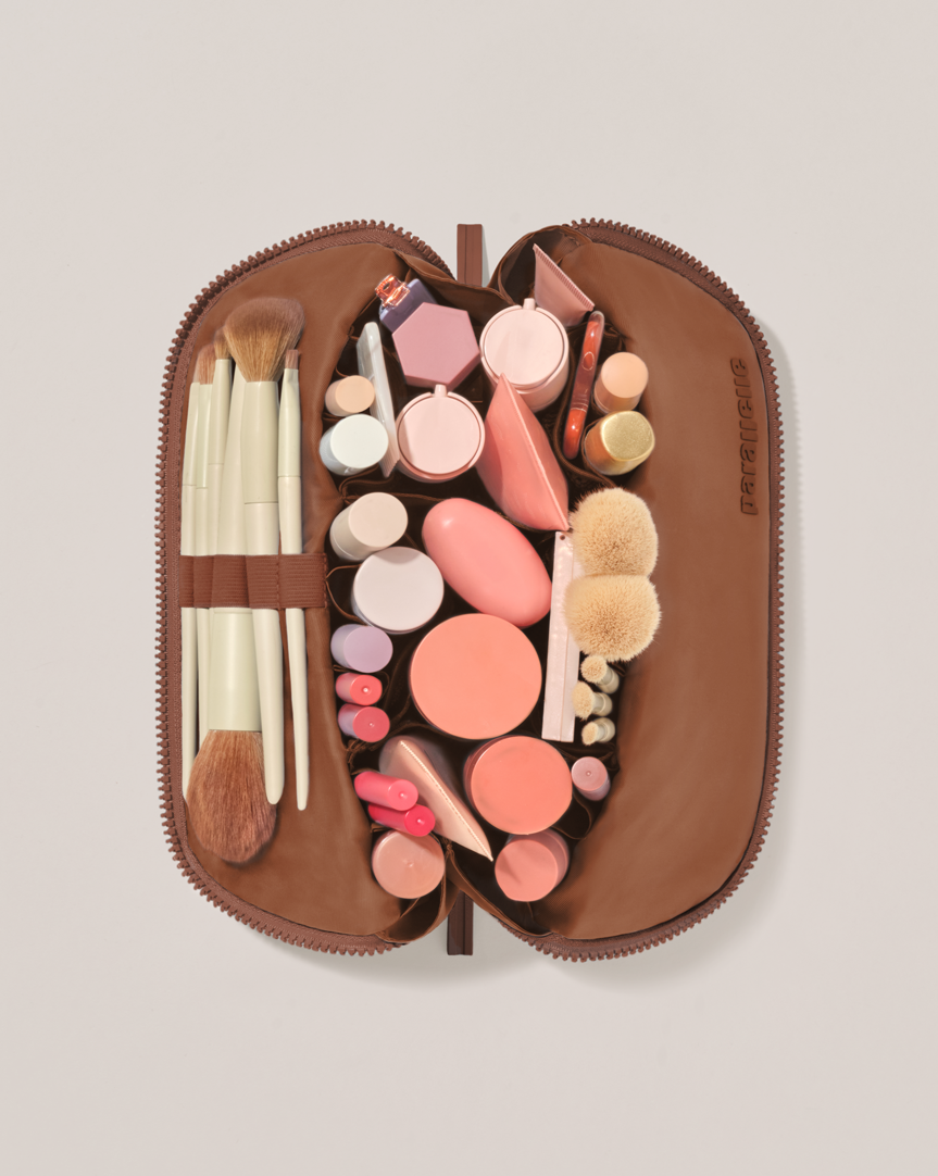 Overhead view of the Medium Vicuna (brown) Traveller makeup bag fully packed with upright beauty products and organized compartments