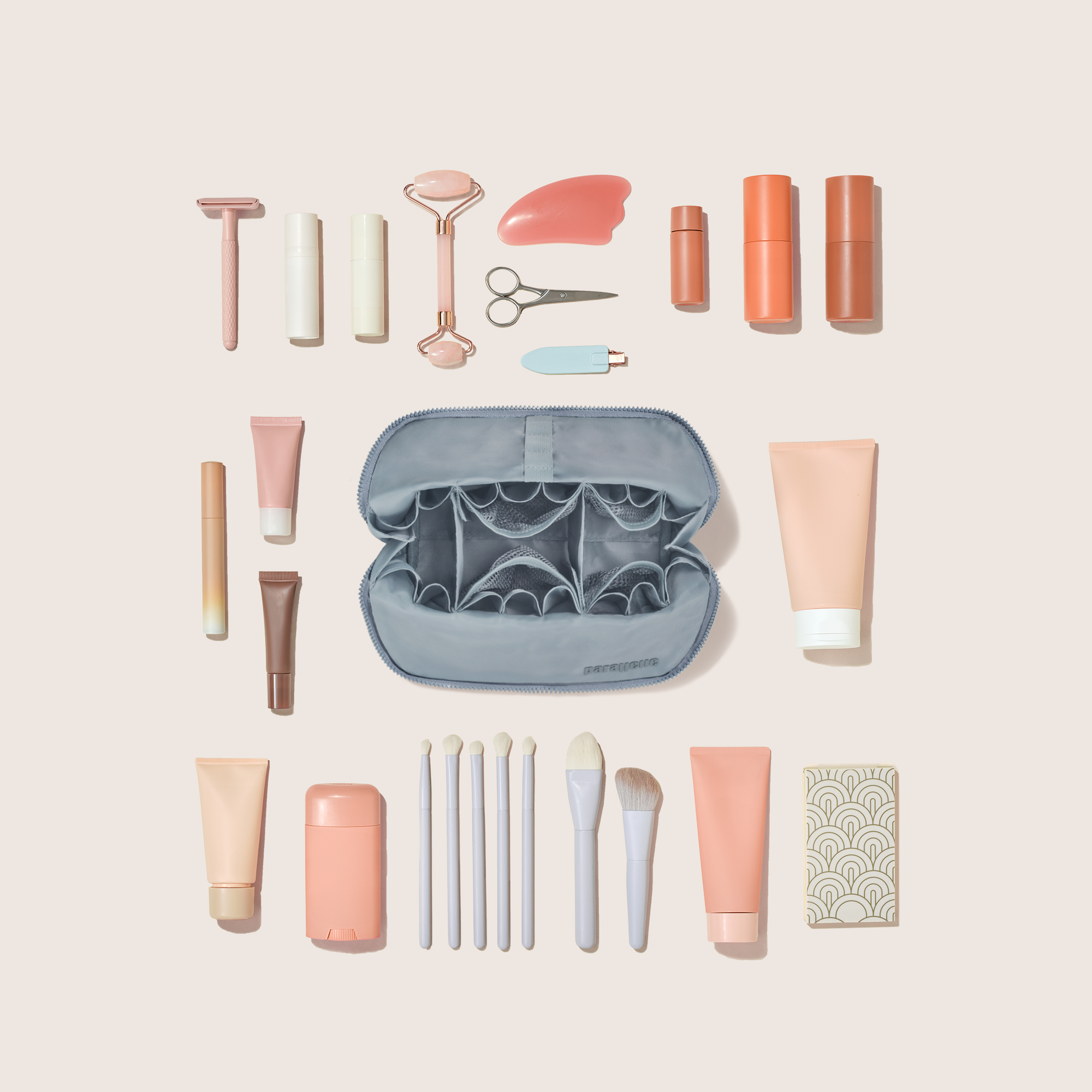 Overhead view of the Medium Slate (blue) Traveller makeup bag showing empty pockets, pouches, and elastic holders and the items that can fit inside it, including makeup brushes, lipstick, face washes, creams, and grooming equipment