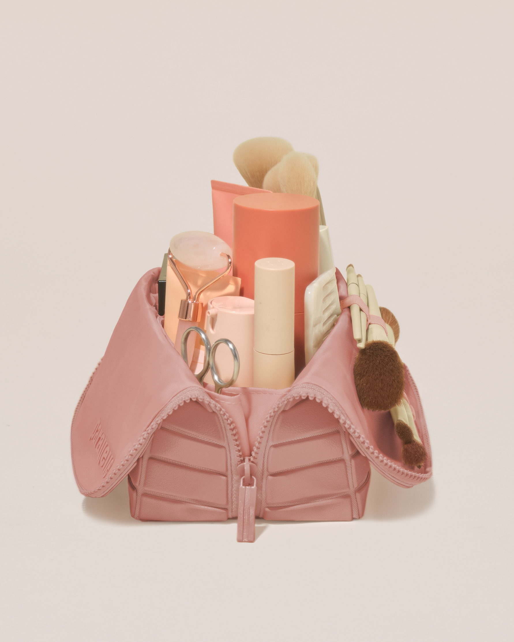Side profile of the Medium Blush (pink) Traveller makeup bag filled with beauty essentials standing upright, showing flexible compartment design
