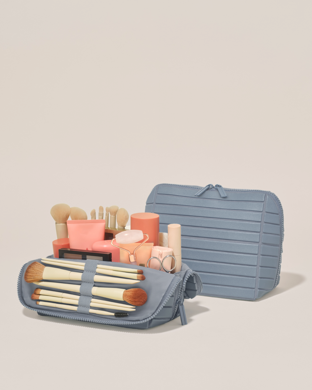 Open and closed Parallelle Medium Slate (blue) Traveller makeup bag showing skincare, brushes, and curated travel essentials