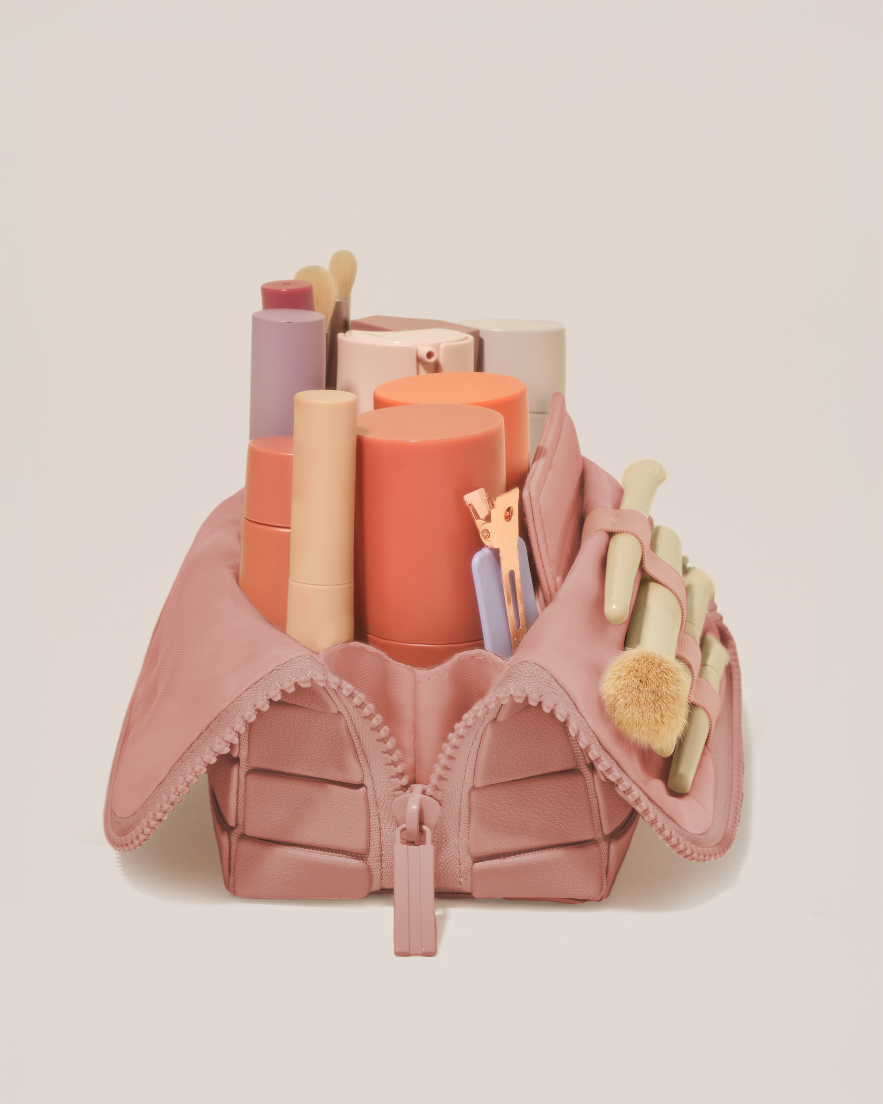 Side profile of the Small Blush (pink) Traveller makeup bag filled with beauty essentials standing upright, showing flexible compartment design